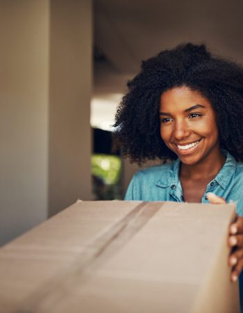 African woman, front door and package for delivery, e commerce and shipping service with happiness at house. Girl, box and smile for supply chain, customer experience and cargo for mail at apartment.